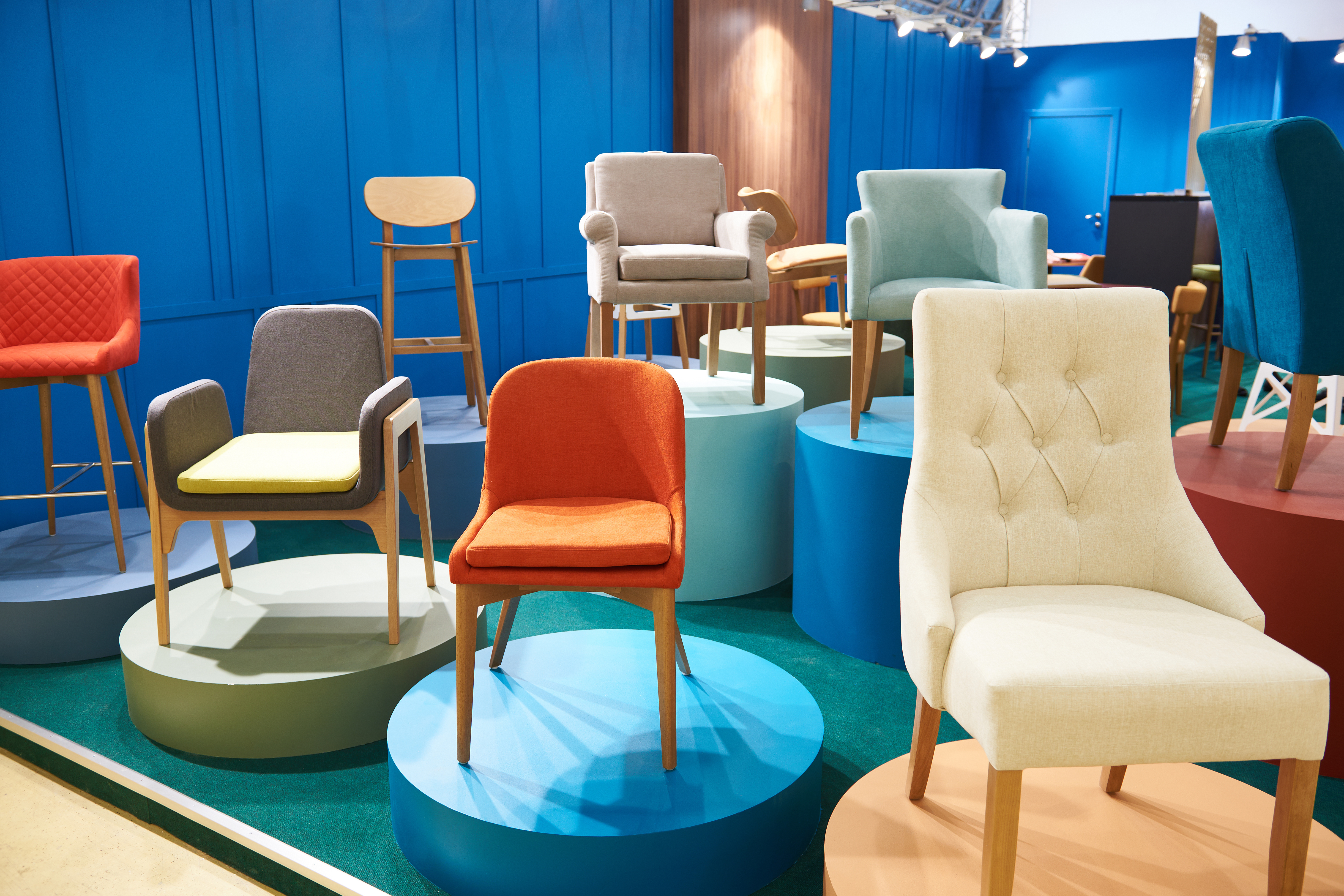 Display of various colorful chairs on platforms in a modern furniture showroom with a blue background